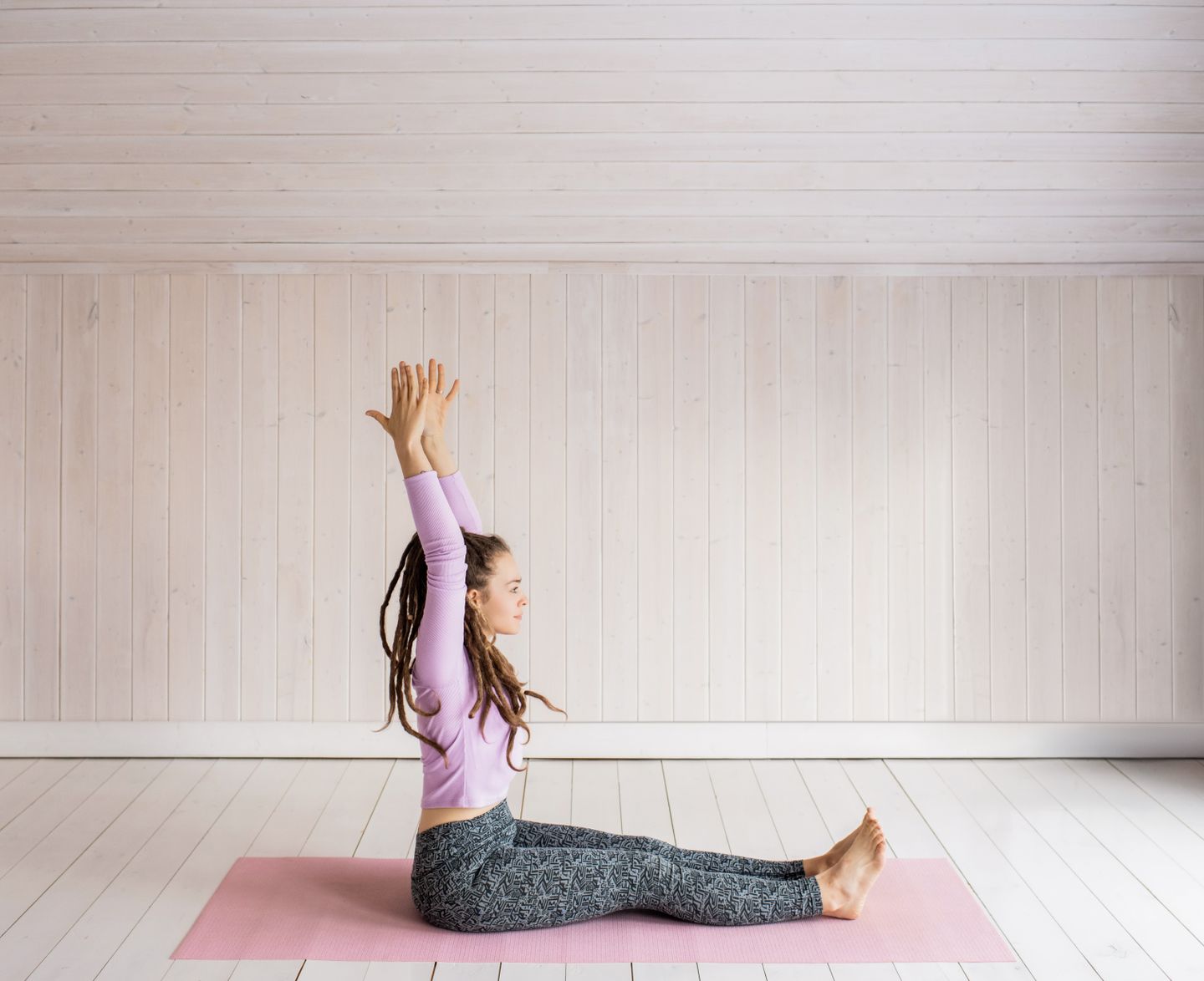Woman performing yoga pose indoors on a pink mat, practicing wellness and mindfulness.